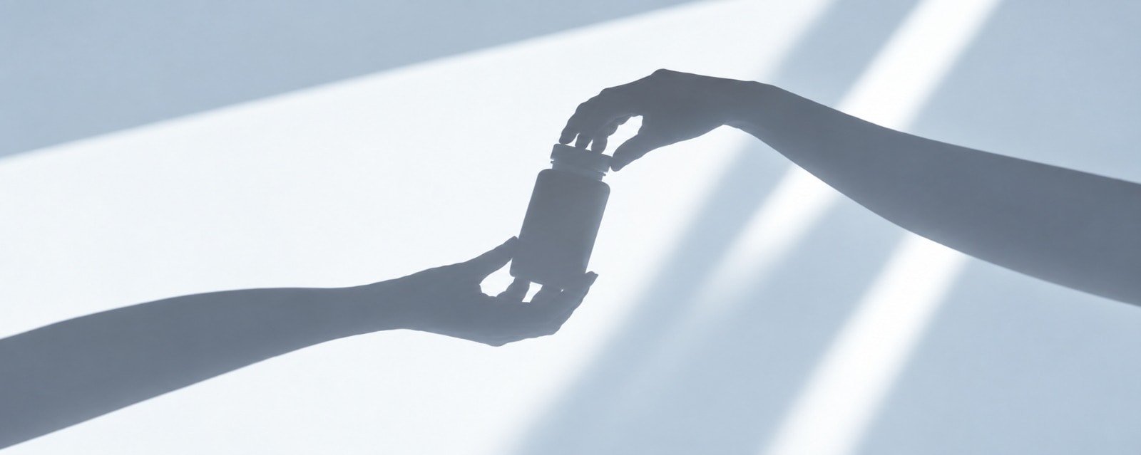 One hand passing a supplement bottle to another, silhouetted in soft daylight.